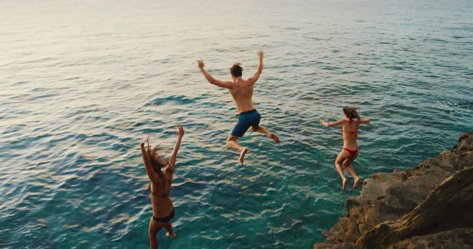 Friends cliff jumping into the ocean at sunset