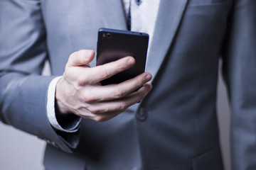 Closeup of sharp looking businessman in grey suit holding mobile phone.