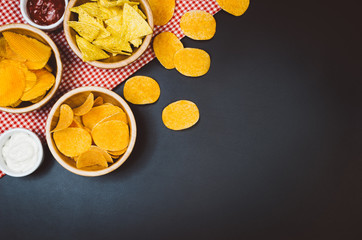 Party snacks - potato chips and snacks in bowl on black slate table. Photograph taken from above, top view with copy space around products.