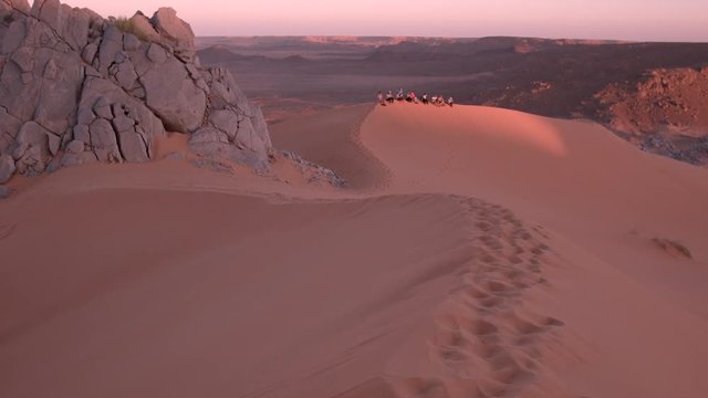 Voyageurs contemplant le coucher de soleil dans le d&eacute;sert du Sahara