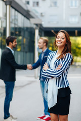 Young businesswoman posing in front of two man shaking hands