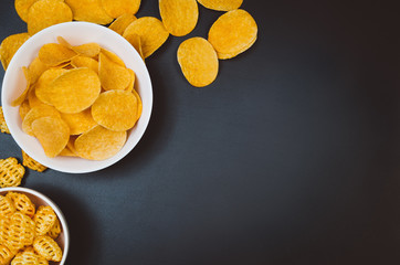 Party snacks - potato chips and snacks in bowl on black slate table. Photograph taken from above, top view with copy space around products.