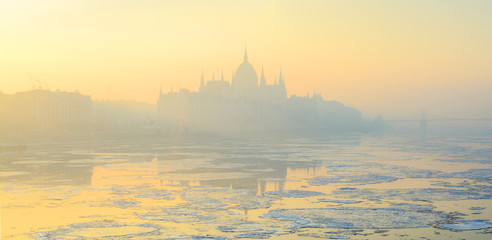 Naklejka premium Panoramic view of Budapest Pest shore with Parliament building in yellow winter haze, Danube river, scattered ice