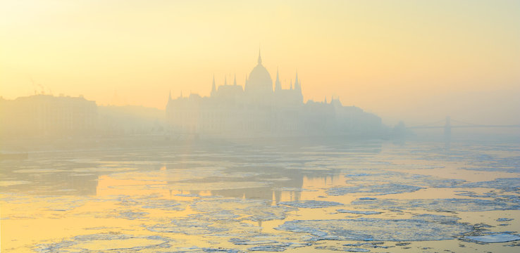 Panoramic view of Budapest Pest shore with Parliament building in yellow winter haze, Danube river, scattered ice