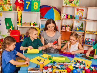 Fototapeta premium School children with scissors in kids hands cutting paper with teacher in class room. Group of children in an orphanage. Children's project in kindergarten. Create animals from paper.
