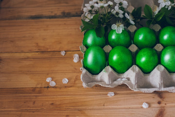 Green Easter eggs in the paper container on the wooden surface with a branch of cherry blossom
