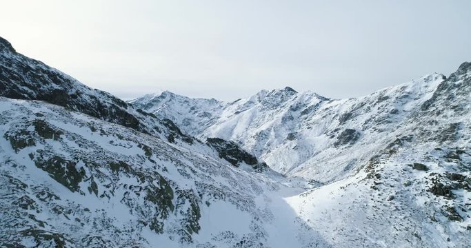 Backward aerial top view over winter snowy mountain rock peaks.Rocky mountains summits covered in snow and ice glacier.Winter wild nature scape outdoor establisher.4k drone flight establishing shot