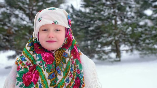 portrait of a child girl in a headscarf in the Urs style on the background of snow and forest. Russia, frost, fairy tale, carnival