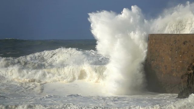 Big wave crashing on jetty slow motion blue sky