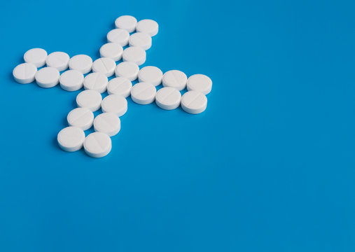 Pill White Round Medications Laid Out In The Shape Of A Cross Or X On A Blue Background