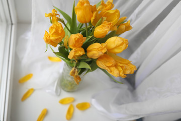 A bouquet of yellow tulips in a vase on the windowsill. A gift t