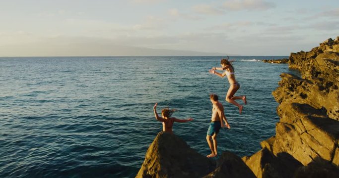 Friends cliff jumping into the ocean at sunset