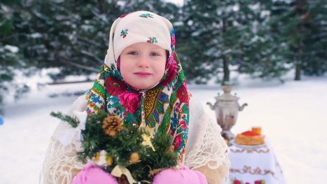 portrait of a child girl in a headscarf in the Urs style on the background of snow and forest. Russia, frost, fairy tale, carnival