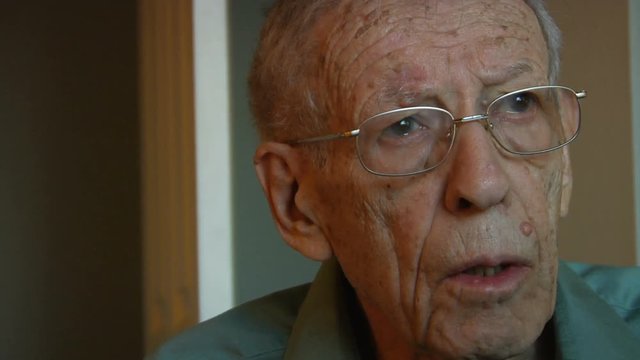 Elderly man watching TV looks down to change channel