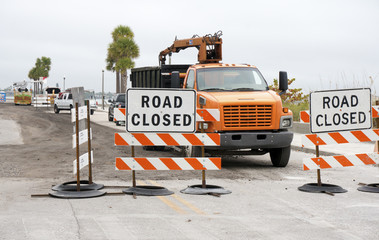 Road construction vehicles prepare to work behind road closed signs.