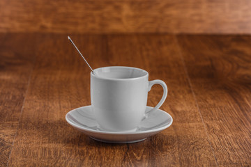 white coffe Cup with spoon on white saucer on dark brown wooden background