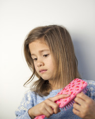 Young girl with far off look while brushing hair with pink brush