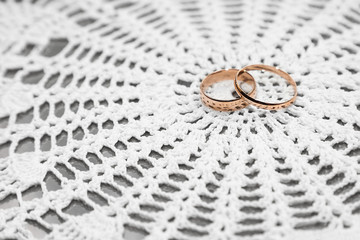 Gold wedding rings on white lace fabric, romantic background, close-up perspective view