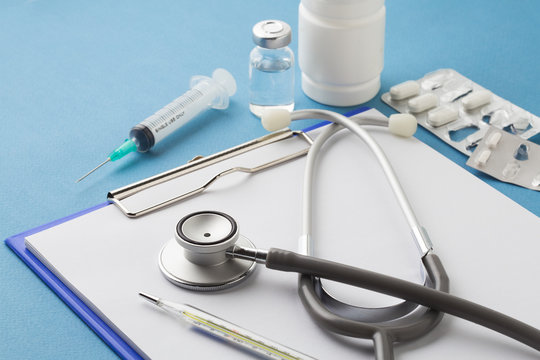Medical equipment : stethoscope ampoules syringe White pills thermometer and stethoscope on blue background