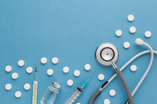 Medical equipment : stethoscope ampoules syringe White pills thermometer and stethoscope on blue background