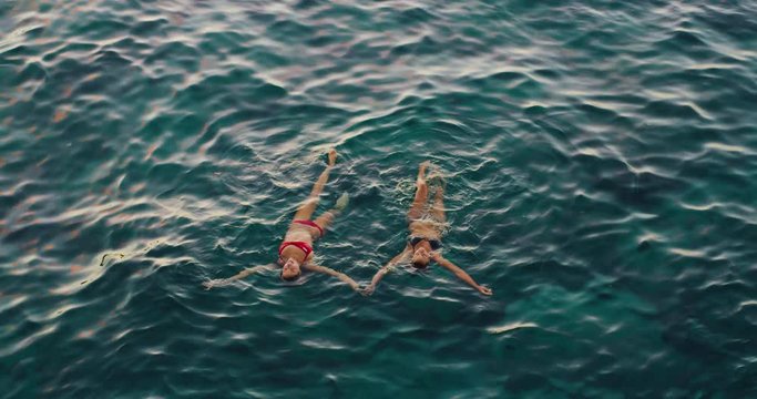 Beautiful girls relaxing floating in the ocean at sunset