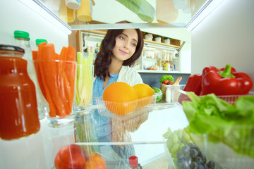 Portrait of female standing near open fridge full of healthy food, vegetables and fruits. Portrait of female