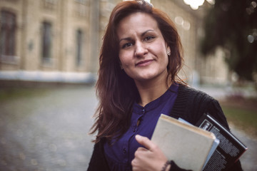 Young female teacher standing on university campus holding books