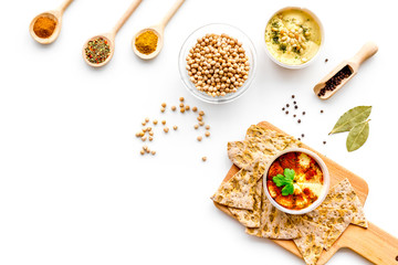 Middle Eastern cuisine. Bowl with hummus among pieces of crispbread and spices on white background top view copy space