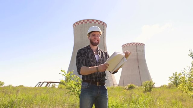 Chief engineer in a white helmet is studying the blueprints on the background of a heat and power plant.