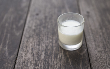 Small glass of organic plain yogurt on wood table. Natural light in a morning. Focus on front of glass. White organic plain yogurt.