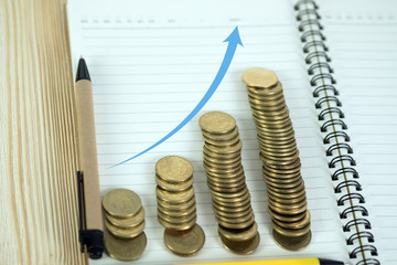 Steps of coins stack with notebook paper on wooden working table with copy space for text, financial and business planning concept.