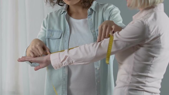 Smiling designer measuring female customer arm, discussing the dress order
