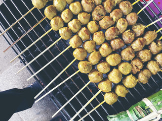 Thai meatballs on a grill on the steel stove on fire at the market. Thai street food. vintage tone.