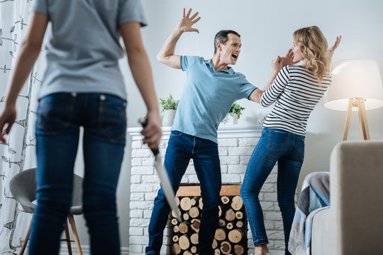 Beating. Determined slim young girl holding a knife and watching her parents while her father beating her mom and shouting