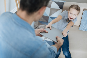 Obraz premium Give me. Angry fair-haired little girl shouting and taking away her laptop while daddy holding it