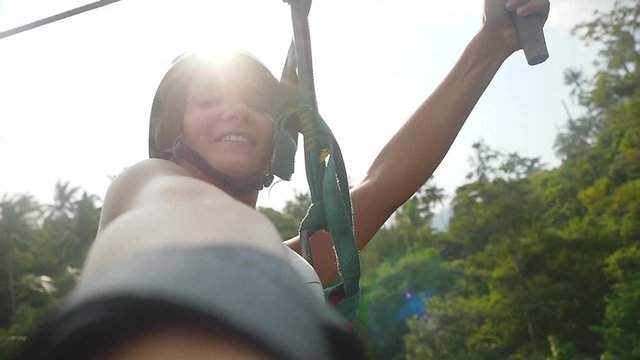 Young happy pretty woman in helmet sliding on high speed zipline rope above beautiful tropic jungle and sunny lights through the forest. slow motion. 1920x1080