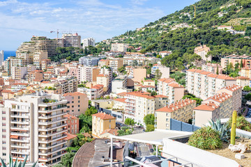 Fototapeta premium Daylight view to tall city buildings, green trees on mountains and blue sea