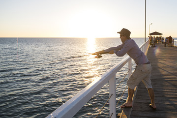 young attractive and happy man in shirt and hat fishing at beach sea dock using fish road enjoying weekend hobby in holidays