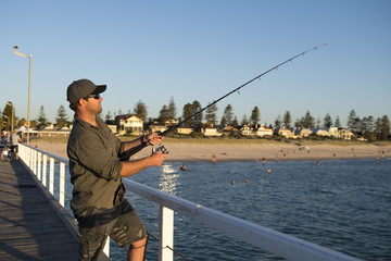 Obraz premium young attractive and happy man in shirt and hat fishing at beach sea dock using fish road enjoying weekend hobby in holidays