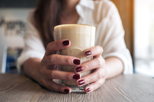 Closeup image of woman's hands with red nails color holding a glass of coffee