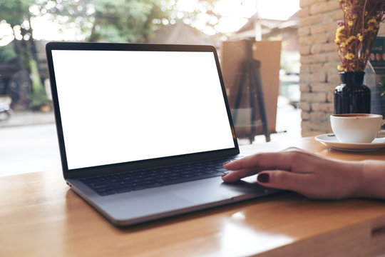 Mockup image of a woman's hand using and touching laptop with blank white desktop screen on wooden table in cafe