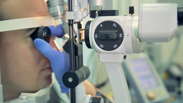 An optician holds a lens to examine the back of the patients eye.  
