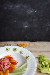 Plate with red fish fillet salad, avocado, celery and cherry tomatoes on a wooden table near the black wall for menus, copy space for your text