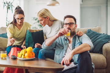 Young women sitting at home with bags after shopping. Young man watching tv.