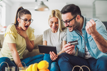 Two women and a man in living room holding credit card and digital tablet