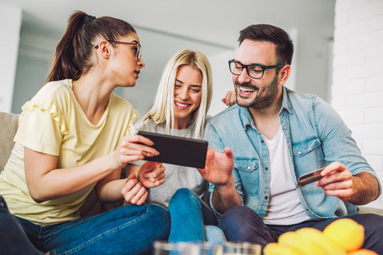 Two women and a man in living room holding credit card and digital tablet - Powered by Adobe