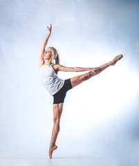 Beautiful female fitness model doing stretches and dancing in a studio, isolated against white background