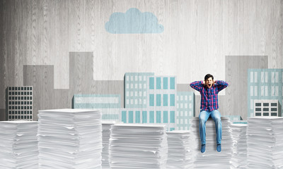 Young man sitting on pile of paper documents.