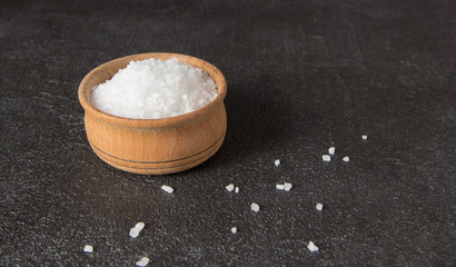  salt in a wooden bowl on dark concrete background