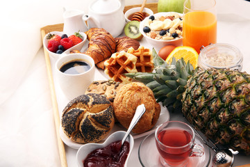 breakfast in bed with fruits and pastries on a tray -waffles, croissants, coffe and juice